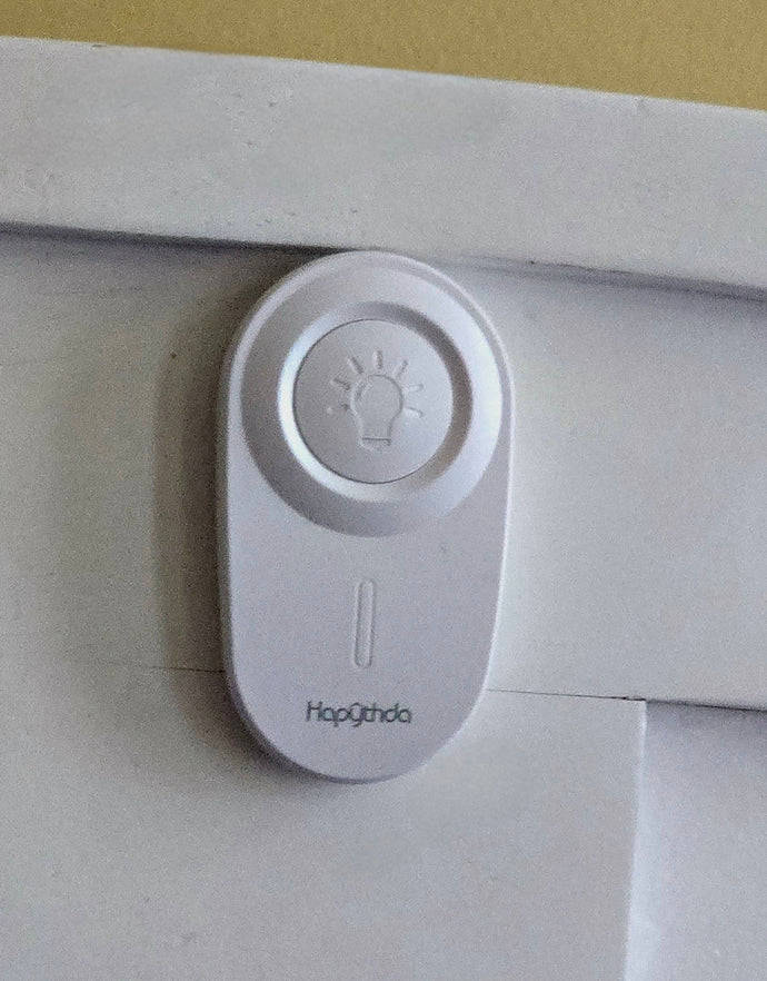 Large white control with a large white button with a light bulb symbol on it attached to a wall. The brand 