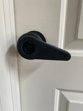 Load image into Gallery viewer, Sammons Preston black rubber extension handle creates a lever on a black round doorknob, on a white door. The key hole is hard to see because it is also black, but there is an opening in the handle for the keyhole.
