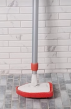 Load image into Gallery viewer, The white scrubber head has a red sponge attached to it, shaped to be able to fit into corners. It has a silver metal pole. Standing straight up on a gray tiled floor with a white tiled wall behind it.
