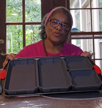 Load image into Gallery viewer, Karen is holding up a baking sheet with four silicone pans on it: 2 larger pans that each take up a third of the tray and then two smaller pans that complete the last third.
