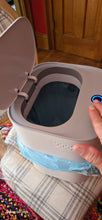 Load image into Gallery viewer, A person has motioned for the trash can to open. The lid is open and a black button or sensor is illuminated with blue light on the top of the device. The trash can opening is smaller than the top of the device, about 3/4 of the size of the device.
