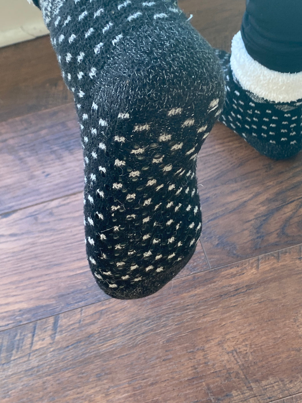 Bottom of a person's foot wearing a black sock with white dots. Grippers are there but not very visible
