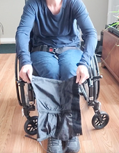 Load image into Gallery viewer, A person in a wheelchair has the gaiter open, with the buckle at the bottom connecting the sides. 
