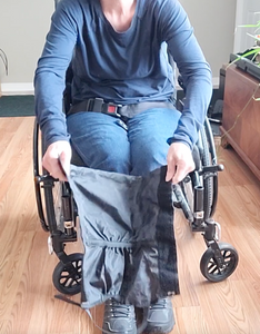 A person in a wheelchair has the gaiter open, with the buckle at the bottom connecting the sides. 