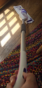 Looking down the rod of the Power Mop. A person is pushing a button at the top to spray solution from the mop head. The mop is on a hardwood floor.