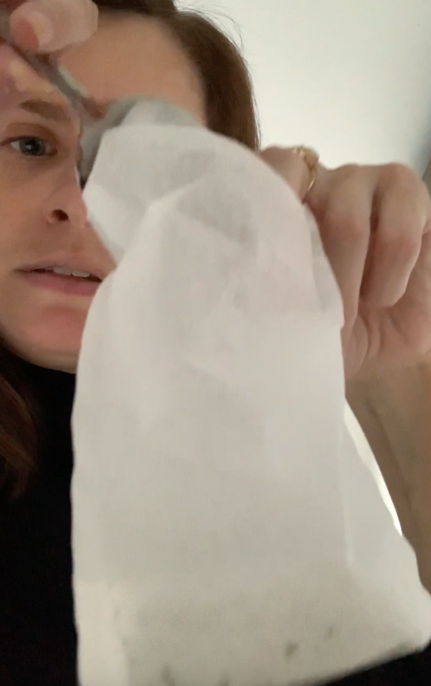 A woman with brown hair uses a spoon to put loose leaf tea in a white tea filter bag