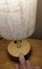 Load image into Gallery viewer, A person touches the lamp on with their finger by tapping the wooden base. The lamp is on.
