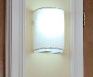 A rounded white wall sconce hanging on a yellow wall between two door frames is lit up.