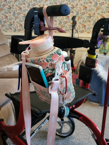 Peach patterned Cube Water Bottle hanging from the handle of a rollator and holding a phone and lotion in its pockets, as well as keys clipped to it.