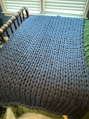 Dark gray chunky knit blanket spread out over the end of a bed.
