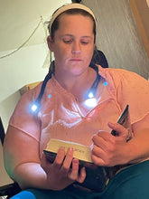 Load image into Gallery viewer, Jessica is reading a book with the slender neck lamp around her neck (shaped like the letter U). Both ends of the device are shining brightly towards the book. 
