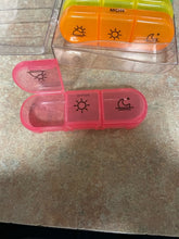 Load image into Gallery viewer, One compartment of the pink pill box is open and the other two are closed. The closed ones show a sun and a moon.
