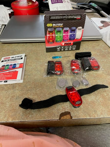 Unwrapped safety light with velcro strap on a counter beside the included batteries, additional lights, mini screwdriver, instruction pamphlet, and box.