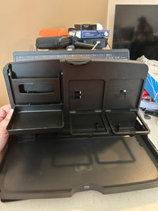 The black organizer is sitting open on a table. It is empty, showing two drink holders, a small compartment, a small tray and a larger tray. 