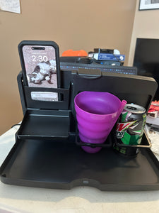 The black plastic organizer is sitting open on a table. It is holding a cell phone, a pink cup and a can of soda.