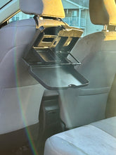 Load image into Gallery viewer, A black plastic tray is hanging from the headrest of a car. The tray is opened, showing various compartments for drinks or other things. The black tray is tilted downward at an angle.
