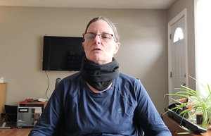 Lisa is wearing a black fleece neck warmer around her neck. It has folds in it, and sits closely around her neck.