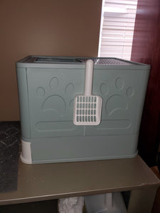 The side of the covered litter box with a white scooper hanging off the side. Imprinted on the outside wall are two large paw prints.