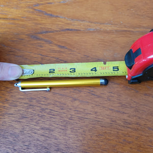 The gold stylus pen is sitting on a table alongside a measuring tape, which shows that it is about four inches long.