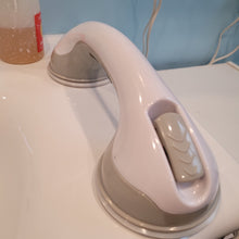 Load image into Gallery viewer, Lisa&#39;s portable grab bar attached to her sink, which is a smooth, non-porous, white, ceramic surface. The bar is white with gray fastening clips and gray around the suction cups.
