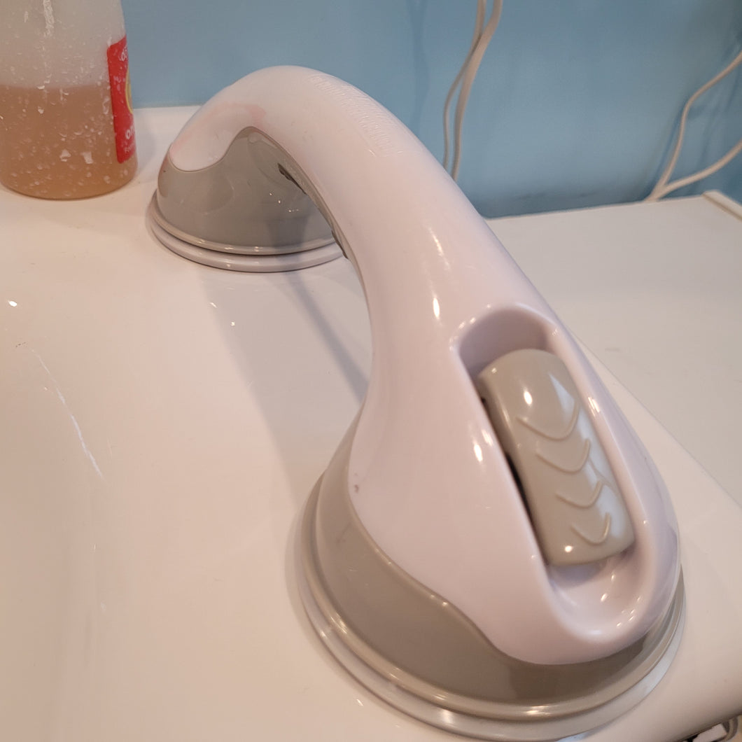 Lisa's portable grab bar attached to her sink, which is a smooth, non-porous, white, ceramic surface. The bar is white with gray fastening clips and gray around the suction cups.