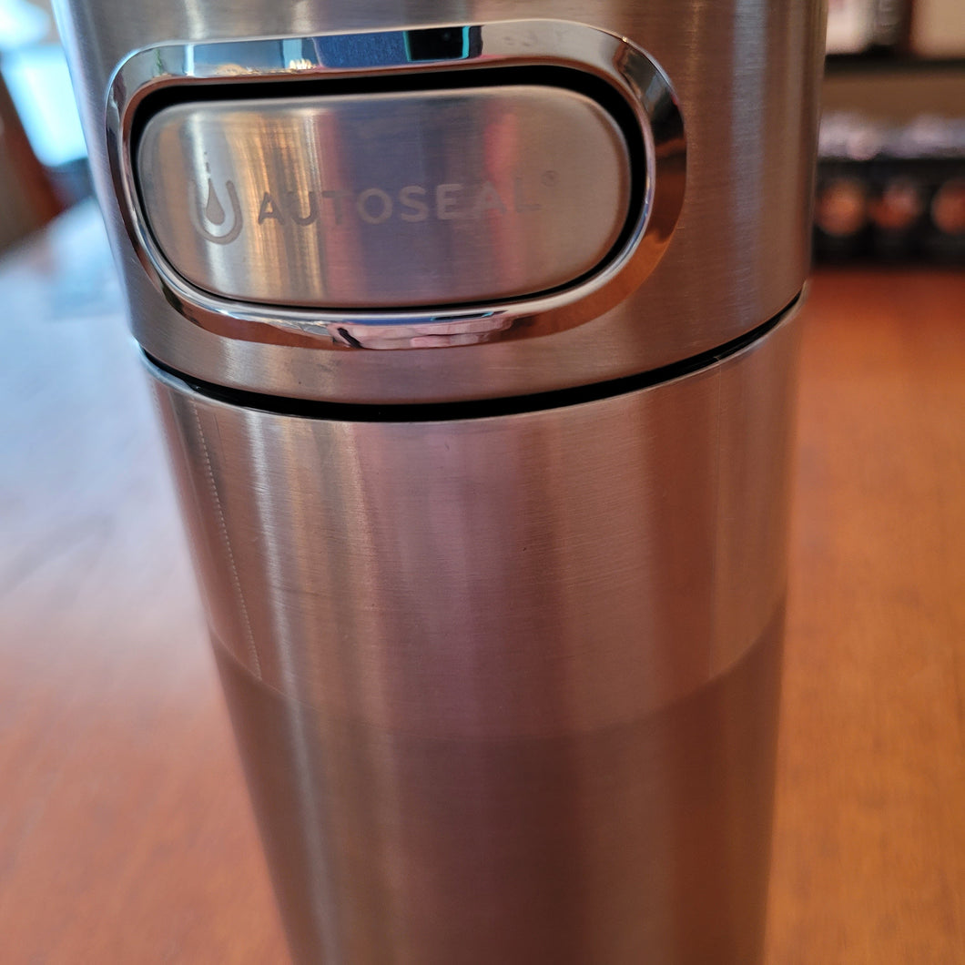 Close up of silver stainless steel Contigo Luxe Autoseal Mug and the button that is used to release the valve for drinking. The button says 