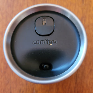 Top of the Contigo mug, showing a black lid with a small drinking hole and a lock button. The lid says "Contigo"