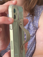 Load image into Gallery viewer, Side view of an olive green phone strap popped out on a phone that a person is holding. The strap is secured by two shiny little knobs that allow the strap to fold down flat or pop up.

