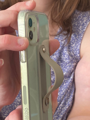 Side view of an olive green phone strap popped out on a phone that a person is holding. The strap is secured by two shiny little knobs that allow the strap to fold down flat or pop up.