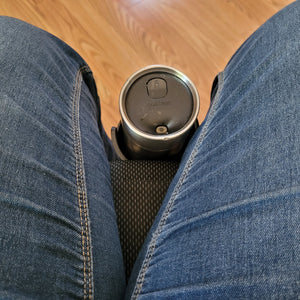 View of a person sitting in the wheelchair, looking down at the cup holder which sits directly against the front of the seat and between their legs. A contigo travel mug is sitting in the cup holder.