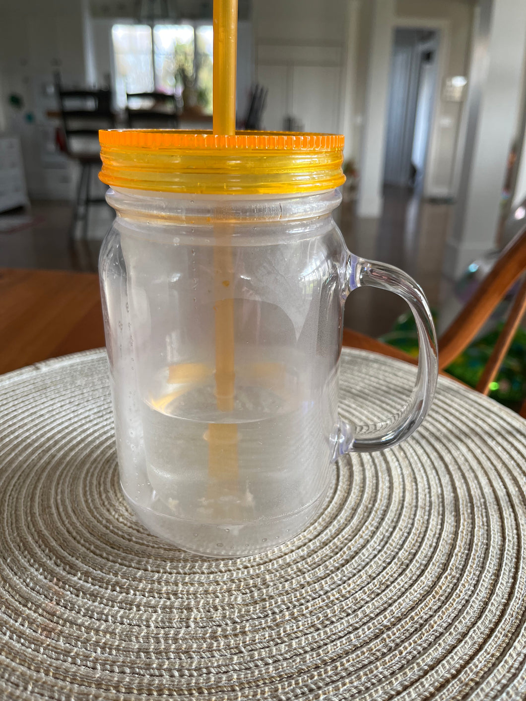 Close-up of clear plastic mason jar cup with handle. The orange straw is visible through the cup. 