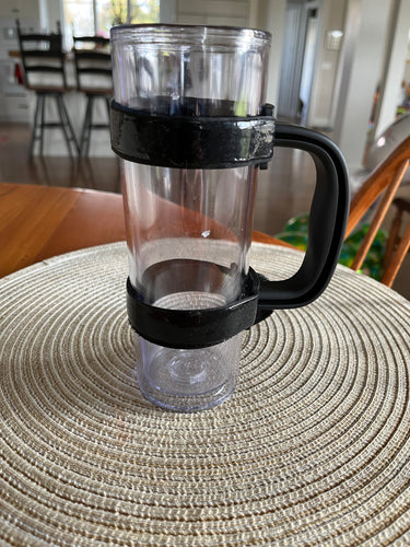 Black adjustable handle is attached to a tall, thin, clear tumbler sitting on a table.