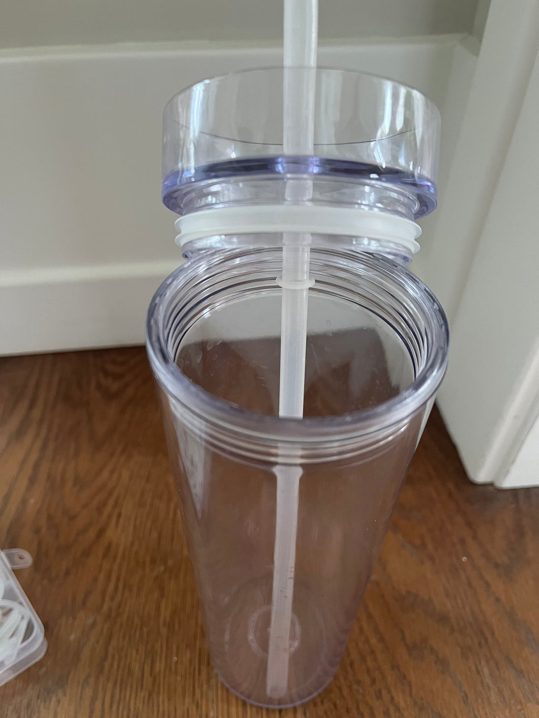Clear tumbler sitting on a wood surface with the lid partially off, showing the rubber seal that holds the lid in place.