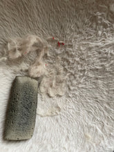 Load image into Gallery viewer, Fur-Zoff pet hair removal tool - which is dark gray and looks like a large, rough stone - is sitting on a white furry cat hammock with visible white pet hair around it. 
