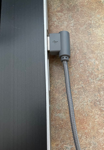 Gray 90 degree iPhone charging cable, plugged into the USB port of a laptop.