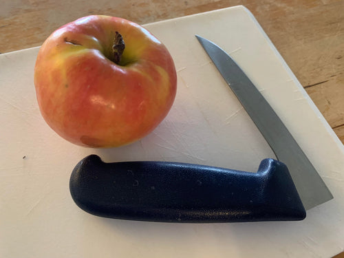 Right angle knife with a stainless steel blade and a dark blue handle sitting on a white cutting board beside an apple.