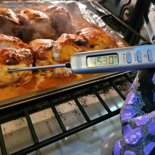 A gray meat thermometer is inserted into chicken cooking in the oven. A pretty large digital screen on the thermometer reads 153.0 F. Three buttons are visible: Power; Hold/CAL; light/Reset. 