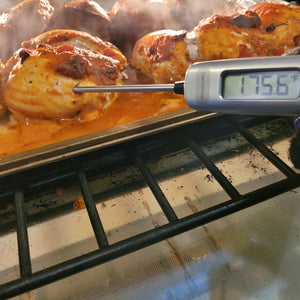 A gray meat thermometer is inserted into chicken cooking in the oven. A digital screen on the thermometer reads 175.6 F.