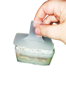 Clear, plastic musubi mold showing a person's hand holding the plunger for the mold