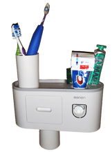 Load image into Gallery viewer, White toothbrush holder creates a small shelf on the wall. Cup sits on the shelf with three toothbrushes in it. On the other side of the shelf are Crest toothpaste (inserted into the toothpaste dispenser), another tube of toothpaste and deodorant. The toothbrush holder has a small drawer and a cup that is magnetized and hanging from the bottom of the shelf. 
