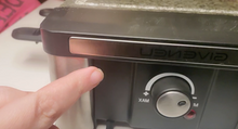 Load image into Gallery viewer, A close up image of a hand pointing to the dial that controls the heat on the grill. It is one knob that turns from M (low) to XAM (high). There is a light beside the knob. 
