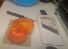 Load image into Gallery viewer, White and gray mandoline slicer on a table with two tomatoes and a knife.
