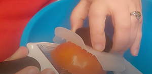Close-up of tomato on the mandoline with a hand holding the non-slip food holder grip