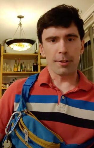 Liam is wearing a red collared shirt with blue, white, and black stripes. The Everest waist bag is being worn across his body and visible in the front, on his chest. His keys are hanging from a zipper with a caribbeaner.