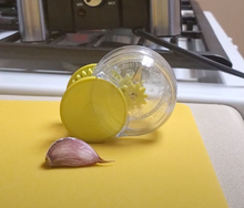 Load image into Gallery viewer, Garliczoom Garlic Chopper sits on a yellow cutting board with a clove of garlic beside it. 

