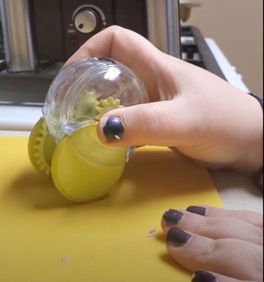 A hand with black nail polish holds the garlic zoom upright to roll it back and forth.