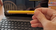 Load image into Gallery viewer, Gold colored stylus pen being held in front of a touch screen tablet. The pen has a black rubber tip.
