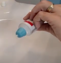 Load image into Gallery viewer, Blue self closing cap on a toothpaste tube being held by a person. There is a dot of toothpaste coming out.
