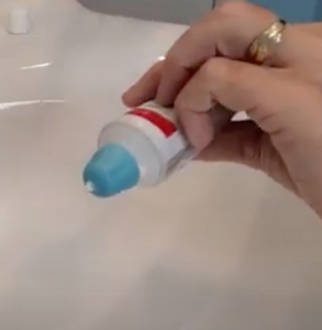 Blue self closing cap on a toothpaste tube being held by a person. There is a dot of toothpaste coming out.