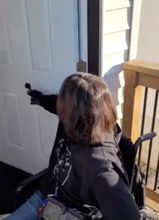 Load image into Gallery viewer, A woman with brown hair, who is a wheelchair user, is using the black door closer to close the front door to a house.
